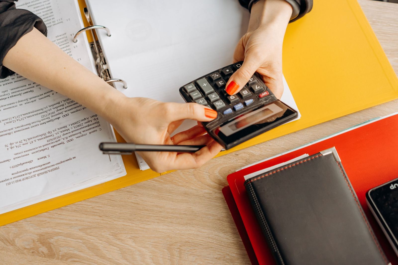 Hands using a calculator over a binder of paperwork